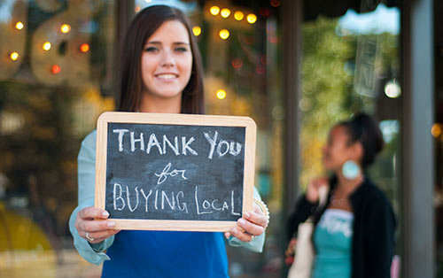 Woman holding a sign that says thank you for buying local